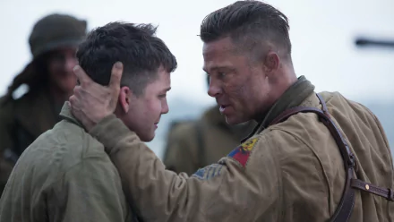 A powerful scene from the movie Fury, featuring Brad Pitt and Logan Lerman, captures an intense moment between the characters against a wartime backdrop.