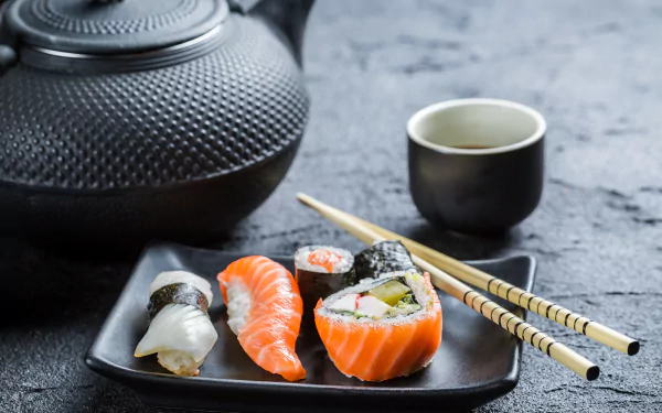 A 4K Ultra HD desktop wallpaper featuring sushi pieces, a black teapot, a small cup of tea, and chopsticks on a textured gray surface.