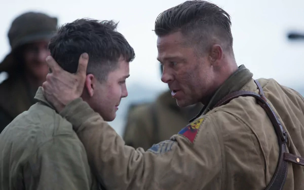 A powerful scene from the movie Fury, featuring Brad Pitt and Logan Lerman, captures an intense moment between the characters against a wartime backdrop.