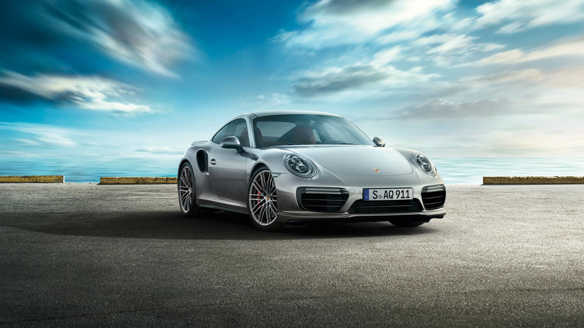 Silver Porsche 911 Turbo on coastal pavement beneath a dramatic sky — 2K Quad HD PC desktop wallpaper and background showing a Porsche 911 sports car.