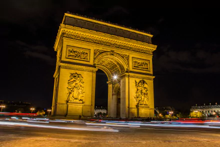 A stunning night view of the Arc de Triomphe in Paris, illuminated by warm light. The image captures vibrant light trails, showcasing the monument's grandeur in a time-lapse effect.
