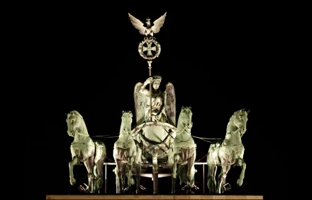 A striking night view of the Brandenburg Gate in Berlin, featuring a majestic statue of a winged figure atop a chariot pulled by four horses, highlighting Germany's historical monument.