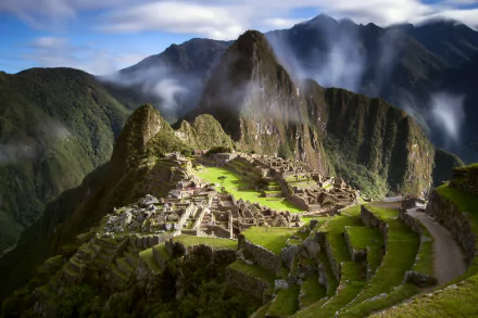 A stunning HD desktop wallpaper of Machu Picchu in Peru, showcasing ancient man-made ruins nestled among lush mountains with clouds drifting across the sky.