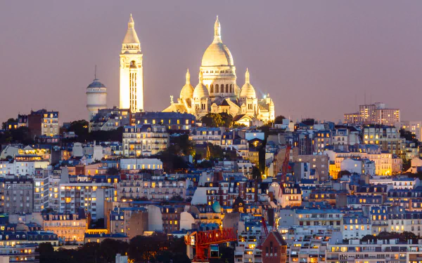HD cityscape of Paris, France at dusk featuring the illuminated Sacré-Cœur Basilica, a prominent religious monument standing above the surrounding buildings.