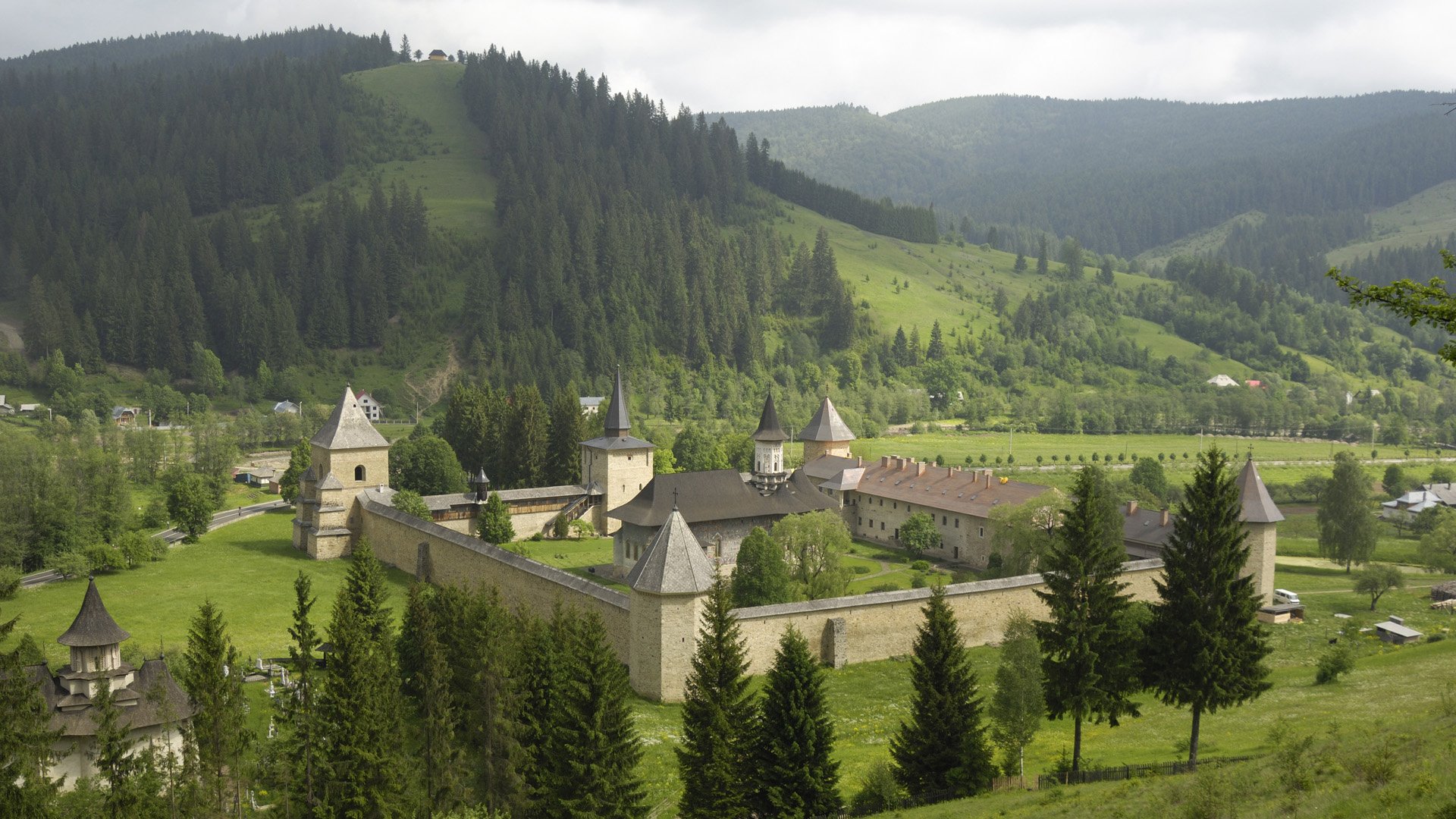HD PC desktop wallpaper: man-made walled monastery building in Romanian hills, surrounded by trees, meadows and rolling green slopes.