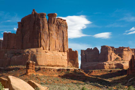 Majestic cliffs rise above the arid landscape of Monument Valley, framed by a vibrant blue sky and wispy clouds, showcasing the stunning beauty of the USA's desert nature.