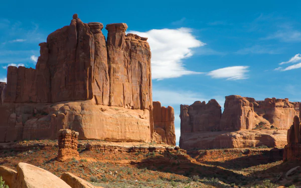 Majestic cliffs rise above the arid landscape of Monument Valley, framed by a vibrant blue sky and wispy clouds, showcasing the stunning beauty of the USA's desert nature.