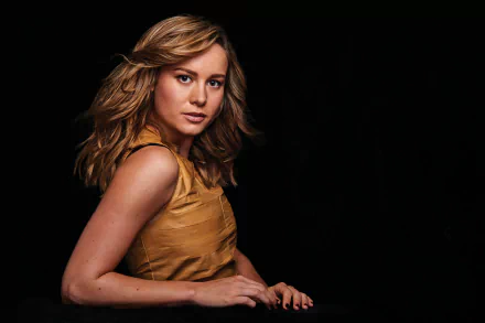 Brie Larson, an American actress with brunette hair and brown eyes, posed elegantly in a striking HD wallpaper against a dark background.