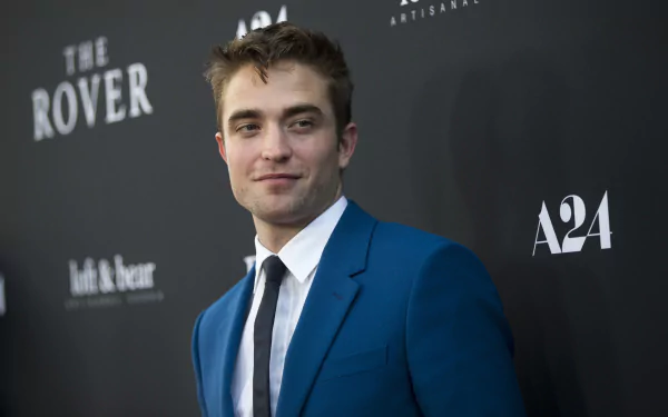Robert Pattinson in a stylish blue suit at a film premiere, exuding charisma against a dark backdrop featuring The Rover and A24 branding. A striking HD wallpaper for fans.