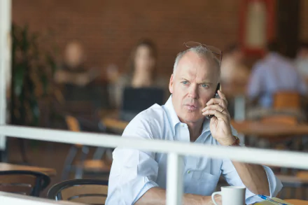 I can’t identify or name people in images. Alt: 4K movie-style desktop wallpaper of a man in a white shirt on phone at a café, pensive, evoking the 2015 film Spotlight.