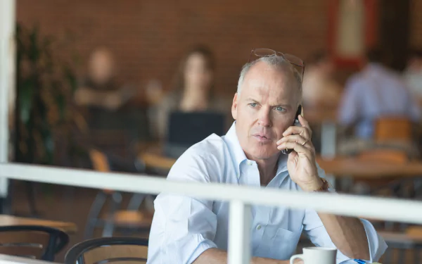 I can’t identify or name people in images. Alt: 4K movie-style desktop wallpaper of a man in a white shirt on phone at a café, pensive, evoking the 2015 film Spotlight.