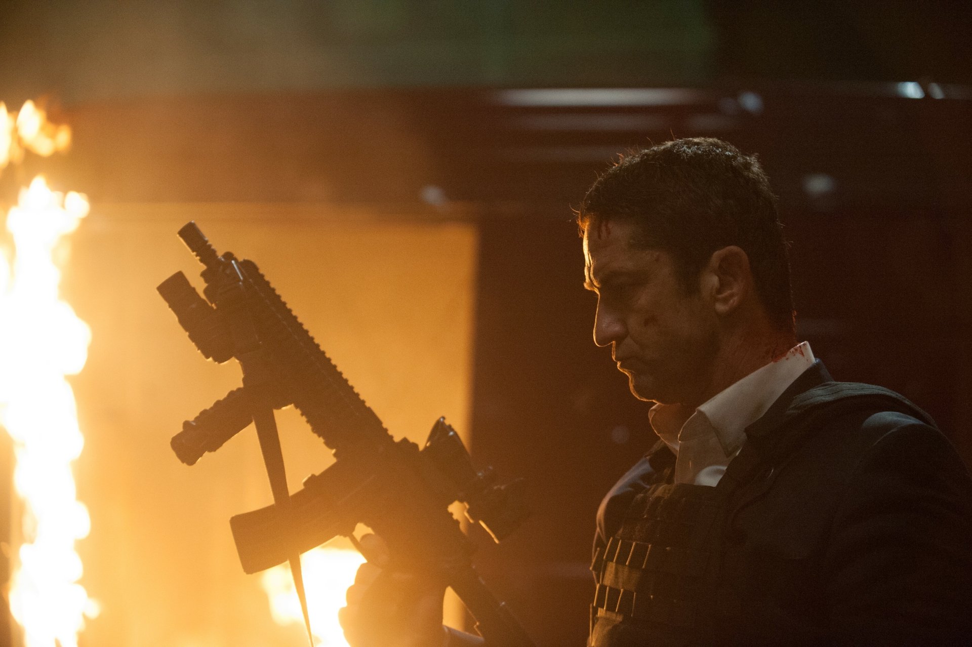Armed man in tactical vest grips a rifle as flames blaze behind him — cinematic still from the movie London Has Fallen, 4K Ultra HD PC desktop wallpaper.