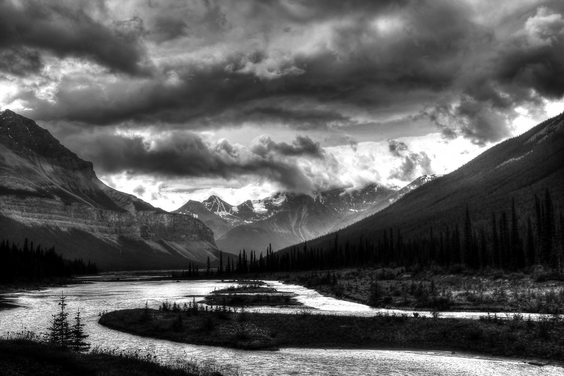 Black and white HD desktop wallpaper of a dramatic mountain landscape with dense forest, winding river, and heavy clouds overhead.