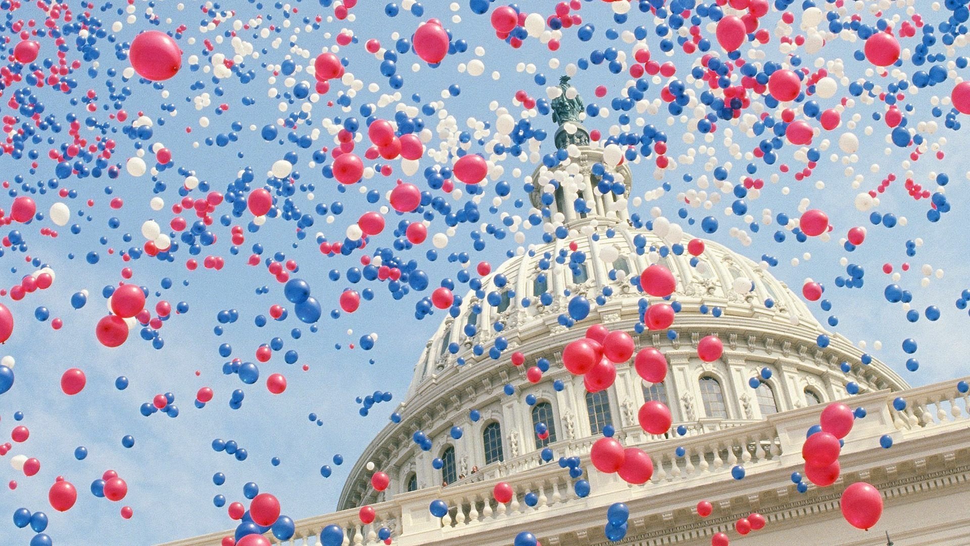 HD desktop wallpaper featuring a 4th of July holiday scene with red, white, and blue balloons filling the sky above a classic capitol building dome.