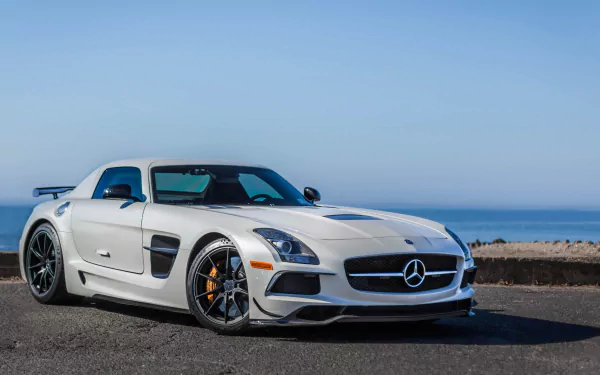 White Mercedes-Benz SLS AMG supercar parked by the ocean under a clear blue sky, showcased in stunning 4K Ultra HD as a PC desktop wallpaper and background.
