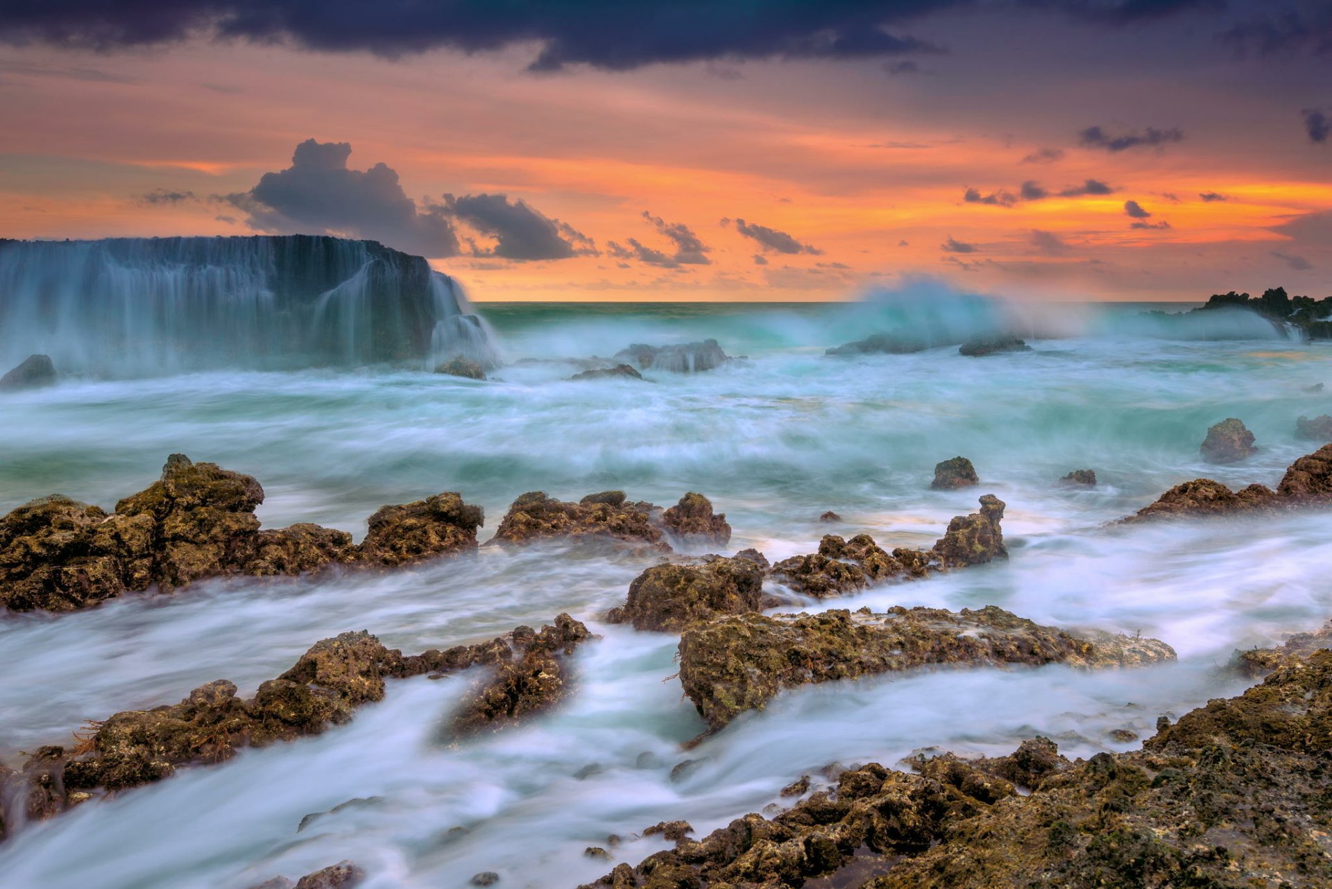 HD desktop wallpaper showcasing a serene ocean at dawn, with rocky shorelines and a vibrant sky meeting the distant horizon in a peaceful natural scene.