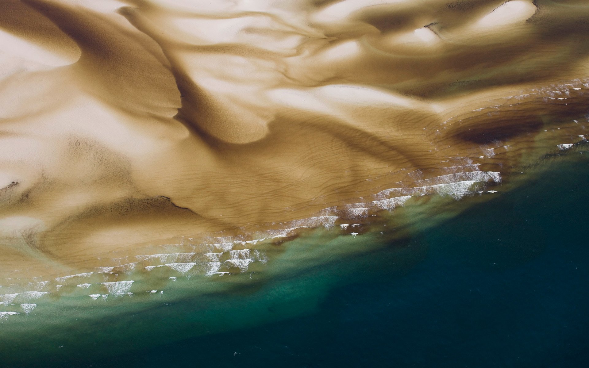 Aerial view of golden sand dunes meeting the ocean in Queensland, Australia, showcasing the beauty of nature with a blend of beach and desert landscapes.