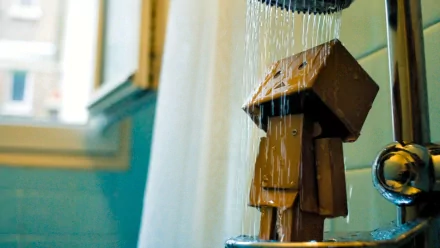 HD desktop wallpaper featuring Danbo, a cardboard robot character, standing under a shower with water streaming down, set in a brightly lit bathroom.