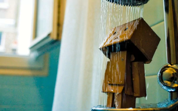 HD desktop wallpaper featuring Danbo, a cardboard robot character, standing under a shower with water streaming down, set in a brightly lit bathroom.