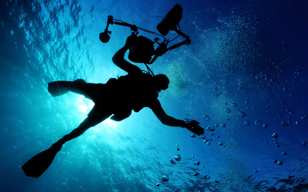 Silhouetted scuba diver with an underwater camera and light, capturing ocean scenes in a vibrant 4K Ultra HD sports scuba diving wallpaper.