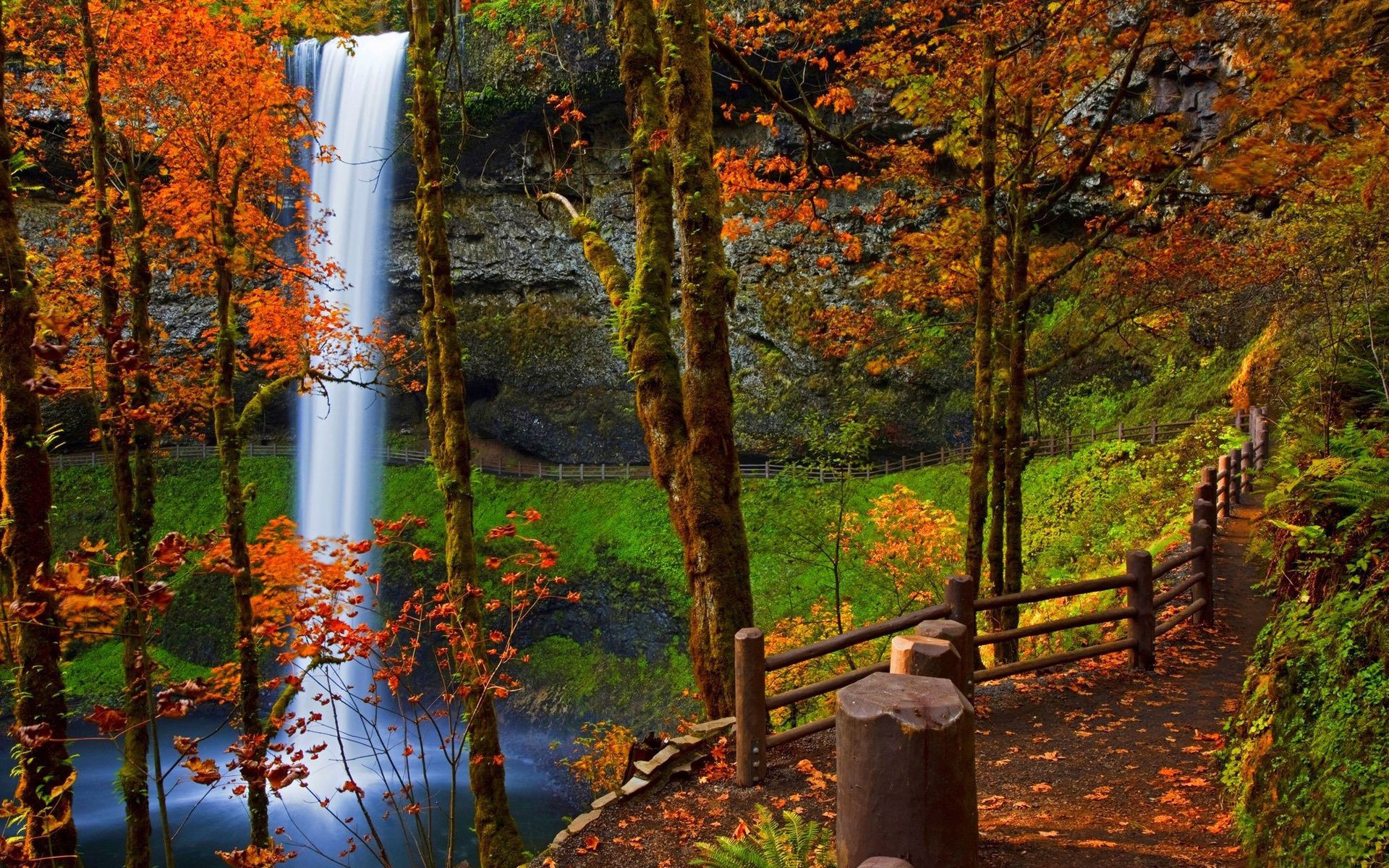 HD PC desktop wallpaper/background: an autumn park with colorful trees and a wooden fence along a path beside a cascading waterfall.