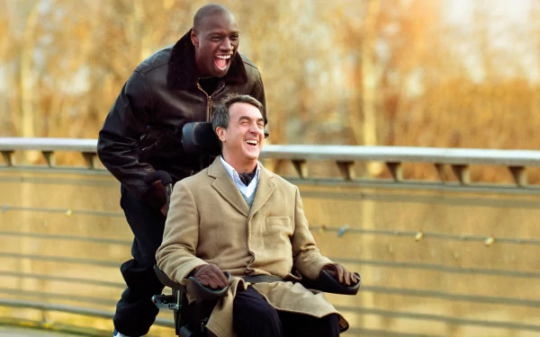 HD desktop wallpaper from the movie The Intouchables: two men smiling on a bridge, one in a wheelchair being pushed.