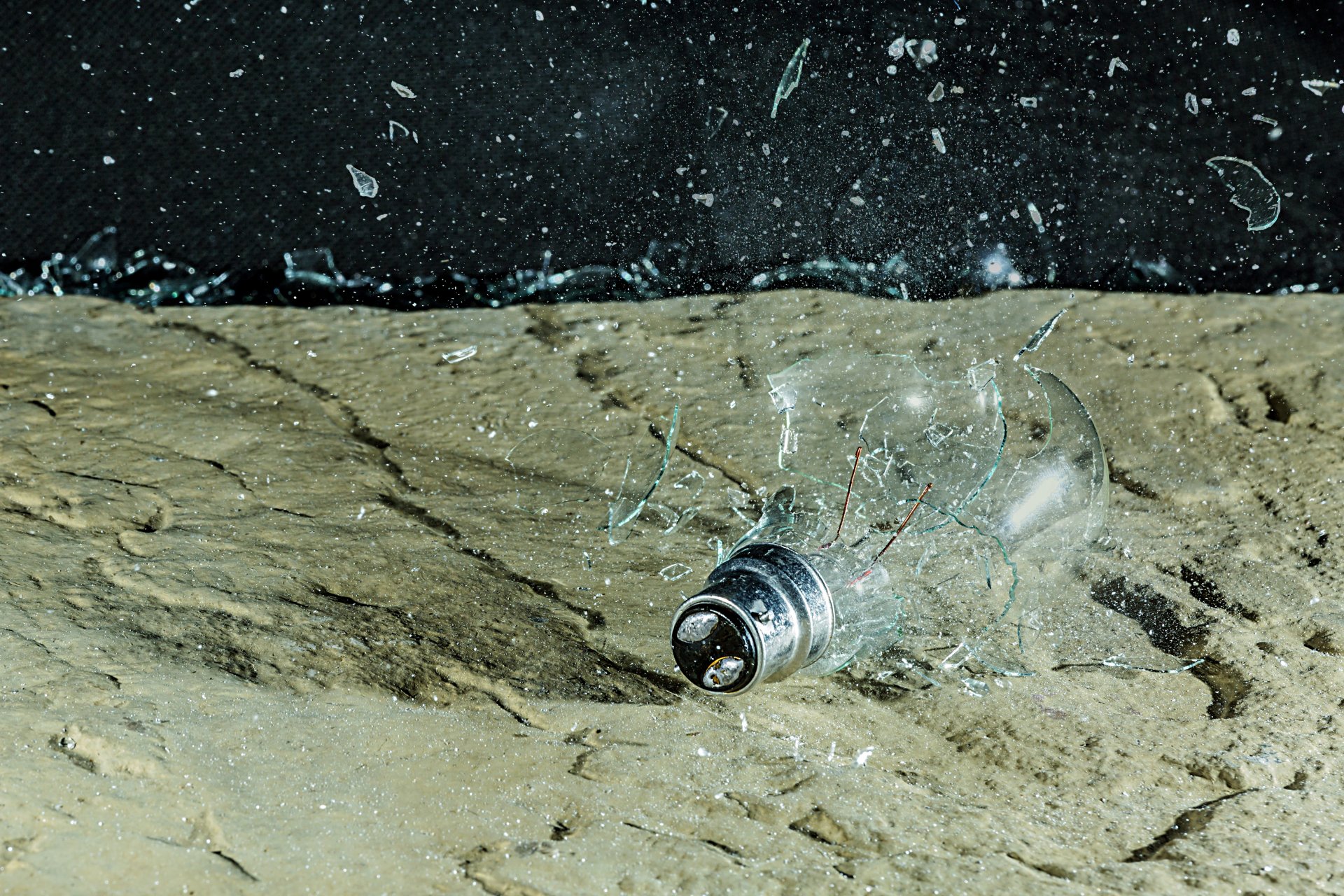 Broken incandescent light bulb amid scattered glass on a rough surface — high-detail 4K Ultra HD man-made light bulb wallpaper and PC desktop background.