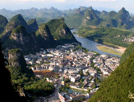 A man-made town nestled among lush karst mountains along a winding river in Yangshuo, China, captured in a stunning HD desktop wallpaper.