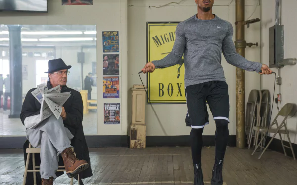 Creed movie 2K Quad HD PC desktop wallpaper: Rocky Balboa seated watching Adonis Creed jump rope in a gritty boxing gym.