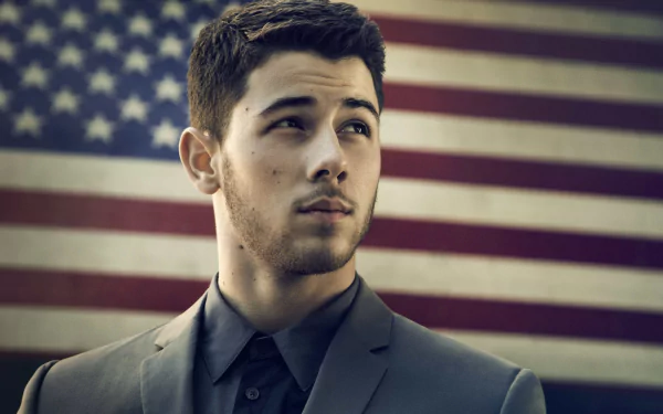 HD desktop wallpaper of Nick Jonas in a suit, with the American flag in the background.