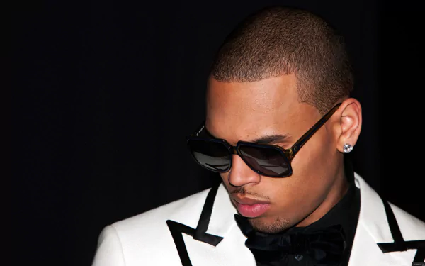 A stylish HD wallpaper featuring Chris Brown in a sharp tuxedo and sunglasses, exuding a confident and cool demeanor against a dark background.