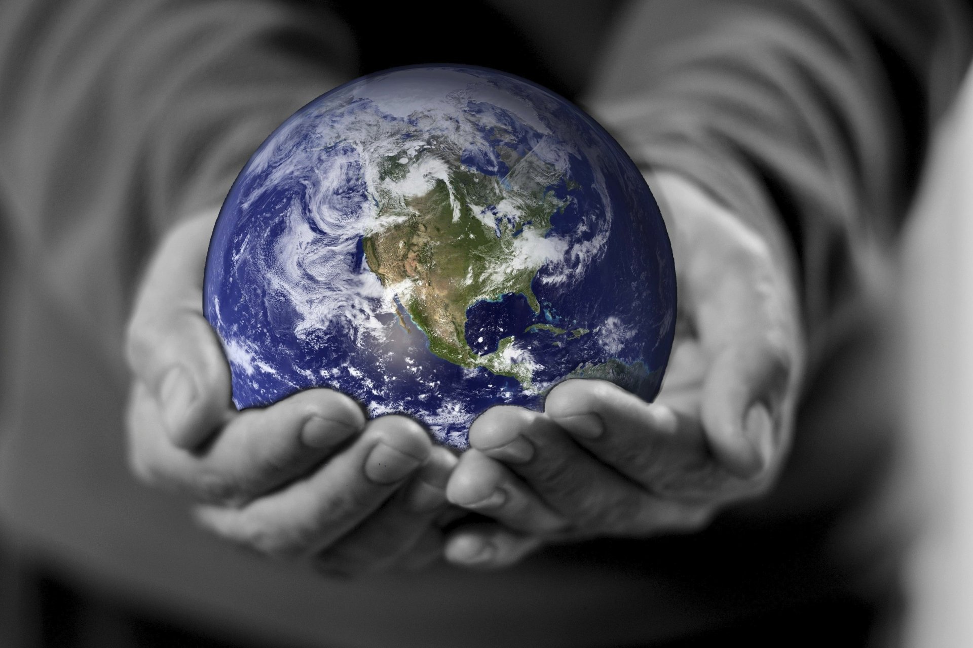 Earth Day holiday 2K Quad HD PC desktop wallpaper and background: vibrant Earth cradled in grayscale hands against a blurred monochrome backdrop.