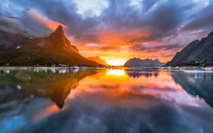 HD PC desktop wallpaper, Lofoten — Reine village at sunset, jagged Norwegian mountains mirrored in a calm lake, vivid earth-toned clouds in dramatic landscape photography.