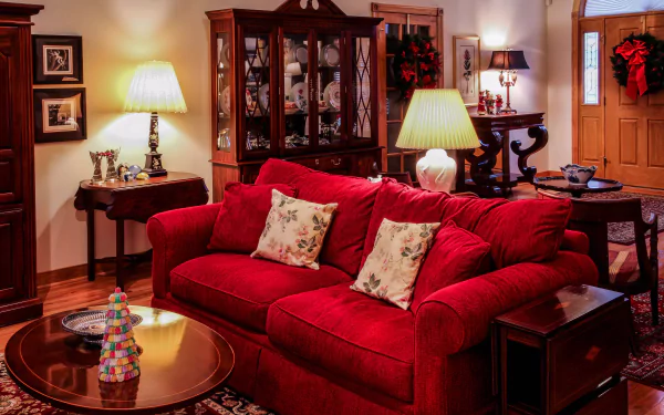 A cozy living room with a vibrant red couch and cushions, warm table lamps, wooden furniture, and festive wreaths, captured in 4K Ultra HD for a PC desktop wallpaper.