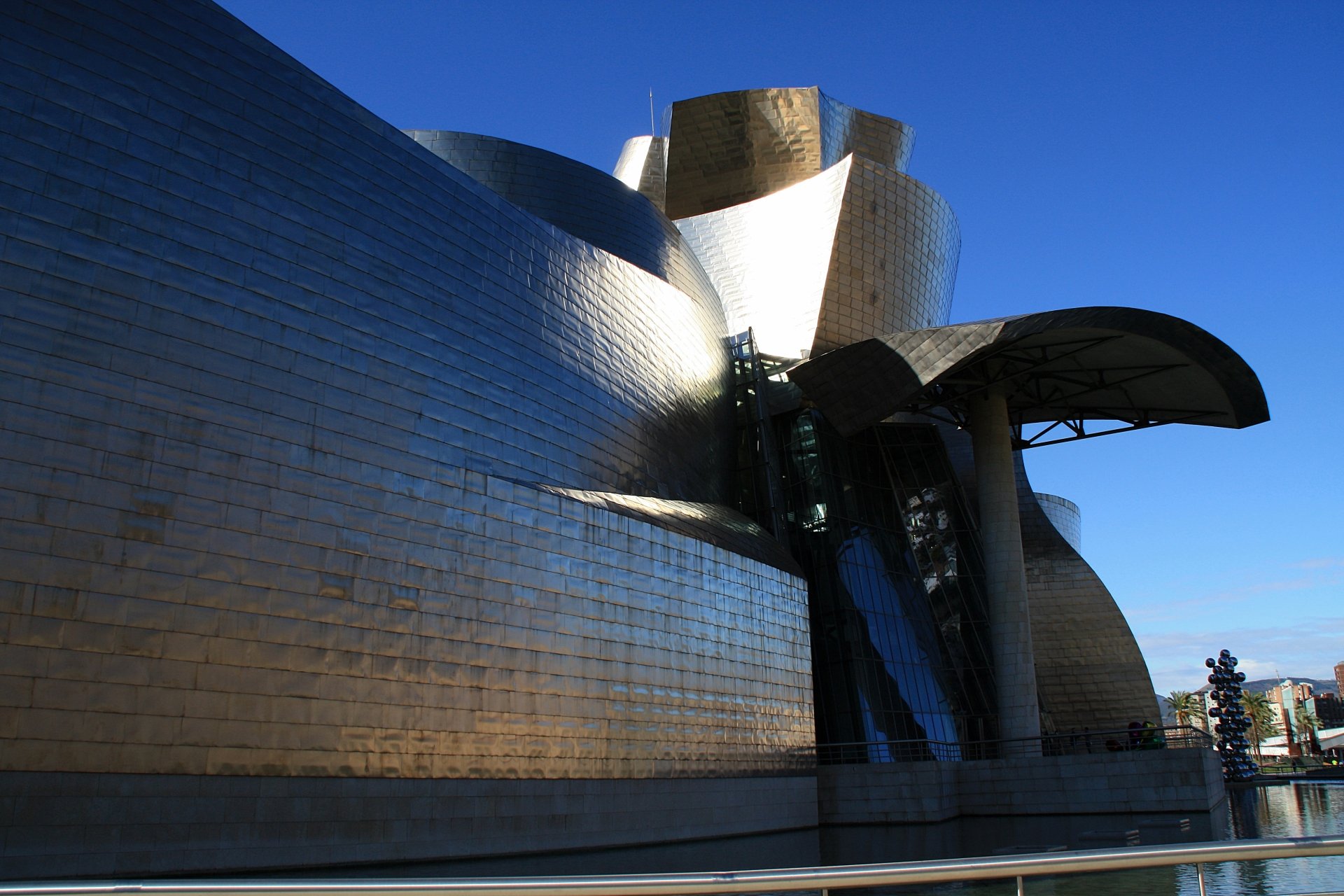 4K Ultra HD image of the Guggenheim Museum in Bilbao, Spain, showcasing its iconic, reflective, man-made architectural design against a clear blue sky.