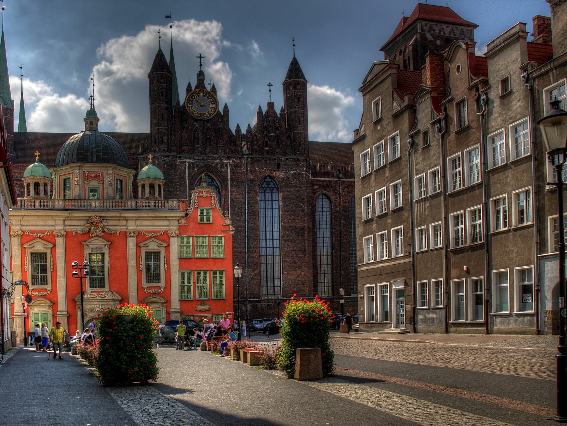 HD PC desktop wallpaper showing a Polish church and courtyard, ornate religious architecture, colorful historic buildings, cobblestone square with planters and pedestrians.