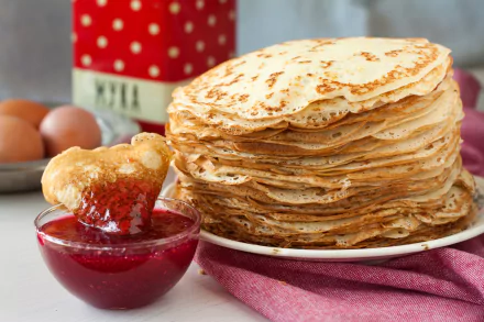 A tall stack of crêpes on a white plate next to a glass bowl of red jam, with eggs and a red container in the background; HD food-themed PC desktop wallpaper.