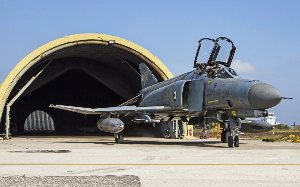 HD desktop wallpaper featuring a McDonnell Douglas F-4 Phantom II jet fighter warplane parked outside a military aircraft hangar.