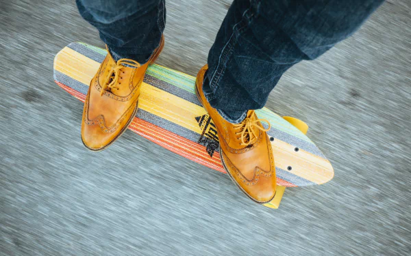 A close-up view of stylish leather shoes on a colorful skateboard, set against a dynamic background, highlighting jeans and the energy of skateboarding sports.