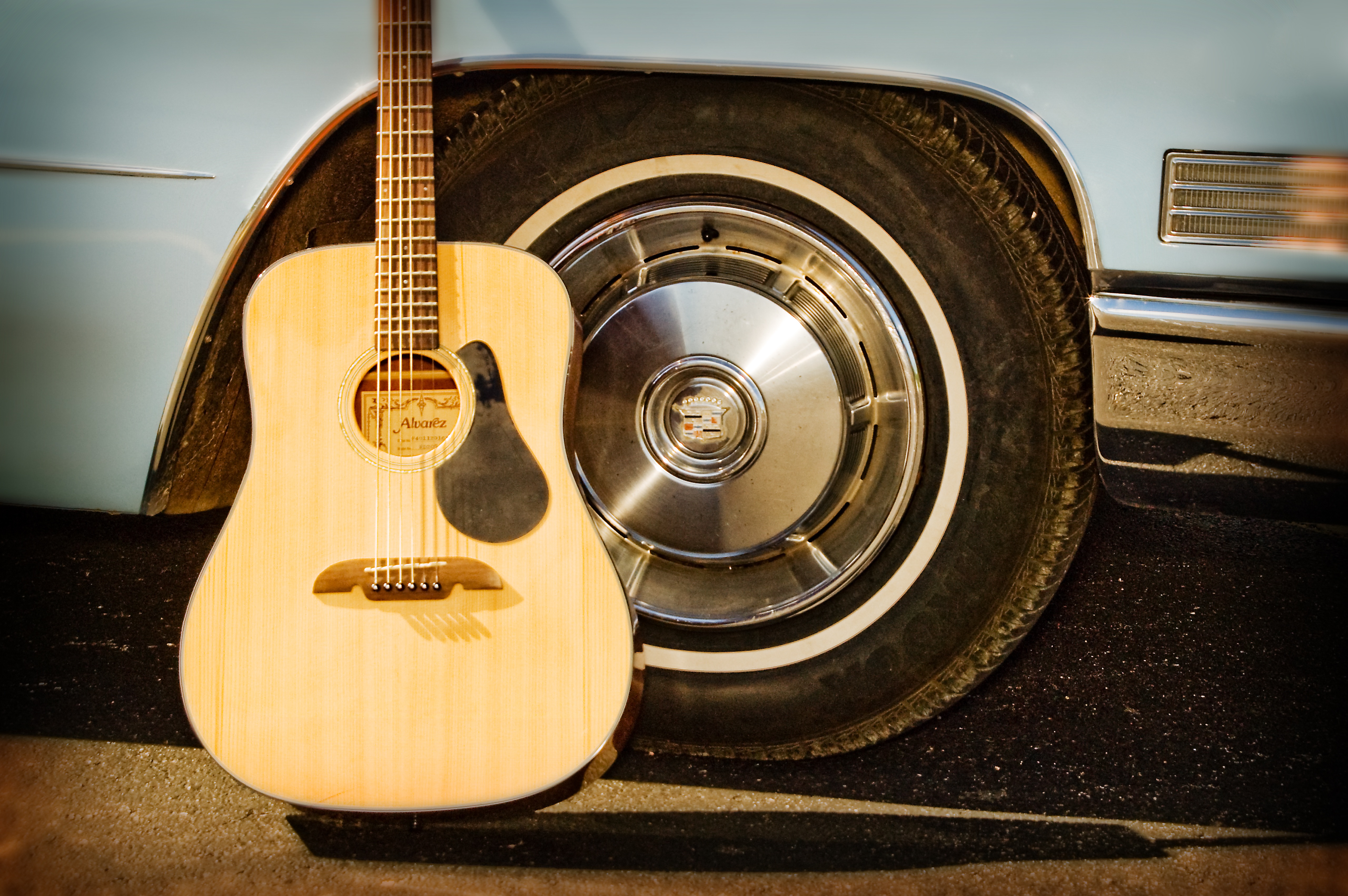 Acoustic guitar leaning up against a car tire by Lisa Johnson