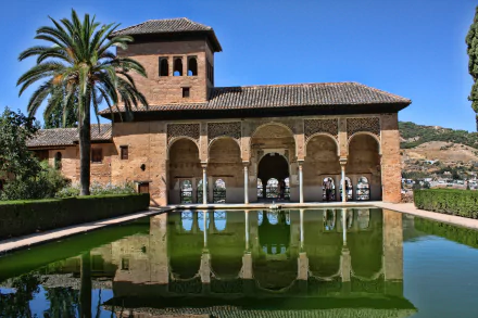 4K Ultra HD image of the man-made Alhambra in Granada, Spain, showcasing its historic architecture reflected in a calm pool under a clear blue sky.