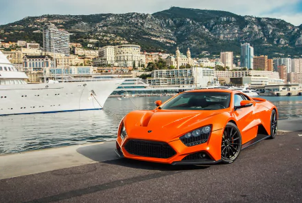 Orange Zenvo ST1 supercar parked by a marina with luxury yachts and city buildings in the background, captured in an HD PC desktop wallpaper and background.