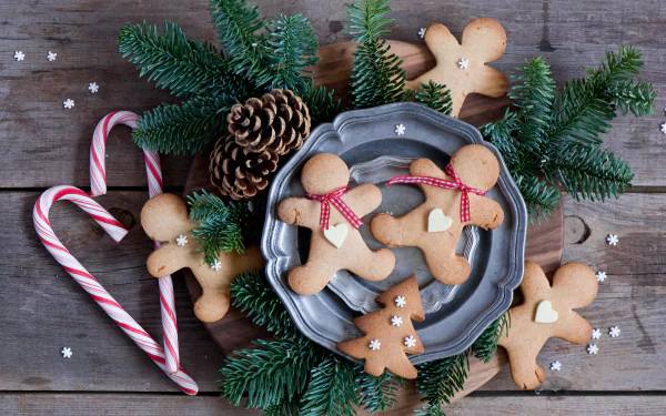 A 4K Ultra HD desktop wallpaper featuring gingerbread cookies, candy canes, pine cones, and evergreen branches arranged on a rustic wooden surface.
