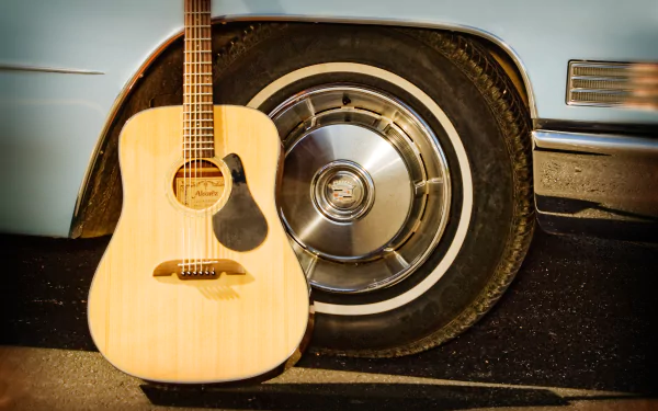 4K Ultra HD wallpaper featuring an acoustic guitar leaning against the wheel of a vintage car, blending musical and automotive elements in sharp detail.