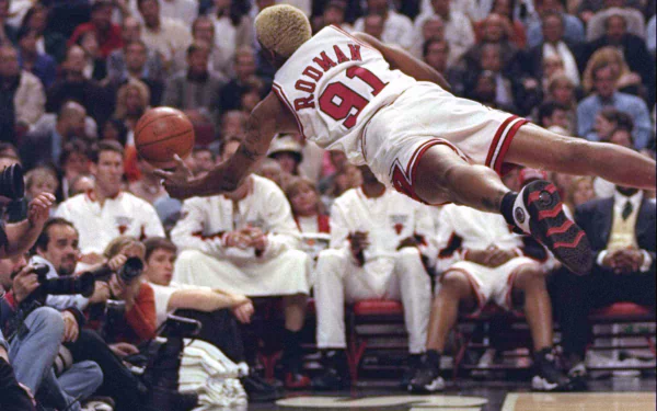 HD wallpaper of Dennis Rodman, in a Miami Heat jersey, diving for a basketball during a game.