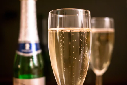 Close-up of two champagne glasses with bubbles, accompanied by a green bottle in the background, captured in 4K Ultra HD for a PC desktop wallpaper.