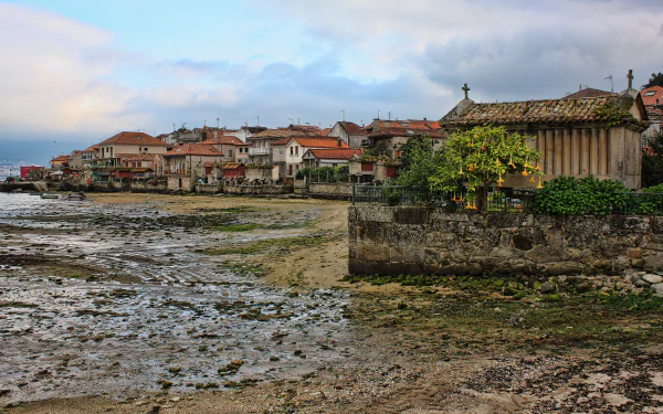 Coastal village in Galicia, Spain, featuring traditional stone buildings along the rocky sea shore under a cloudy sky, captured in 4K Ultra HD.