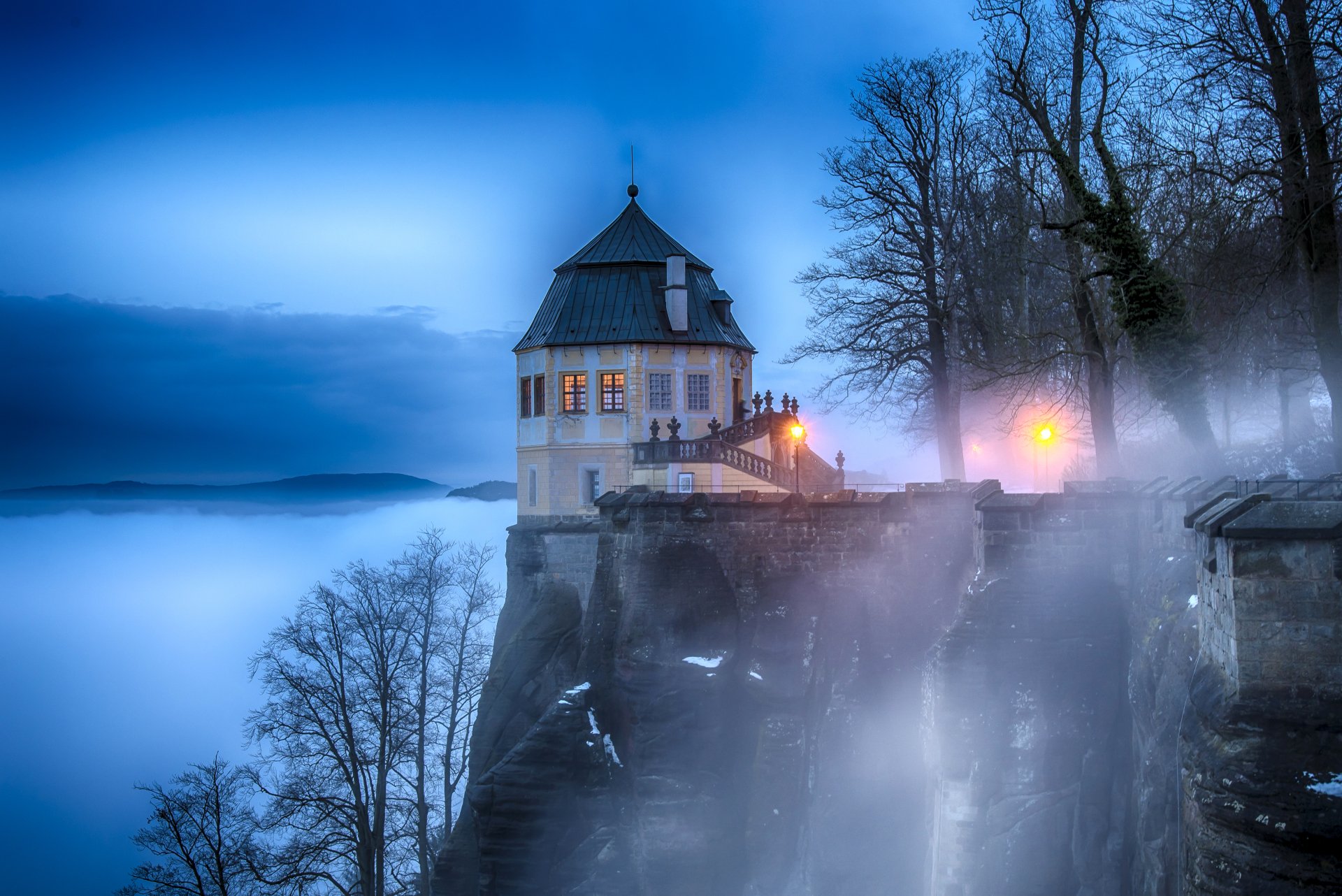Fog envelops the historic Königstein Fortress in Switzerland, creating a mystical atmosphere around the man-made castle in this 4K Ultra HD desktop wallpaper.