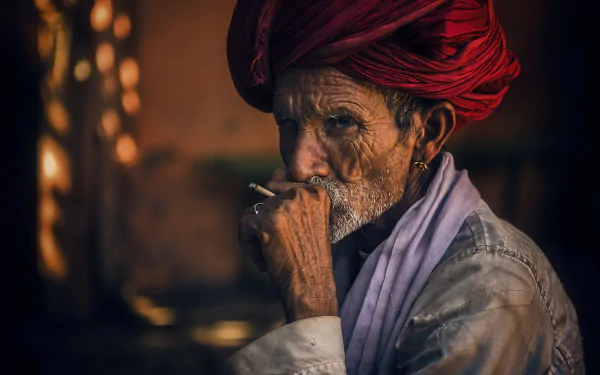 A man with a red turban smokes a cigarette, showcasing a moment of contemplation. This HD wallpaper captures the essence of smoking culture through striking photography.