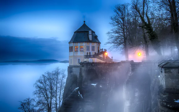 Fog envelops the historic Königstein Fortress in Switzerland, creating a mystical atmosphere around the man-made castle in this 4K Ultra HD desktop wallpaper.